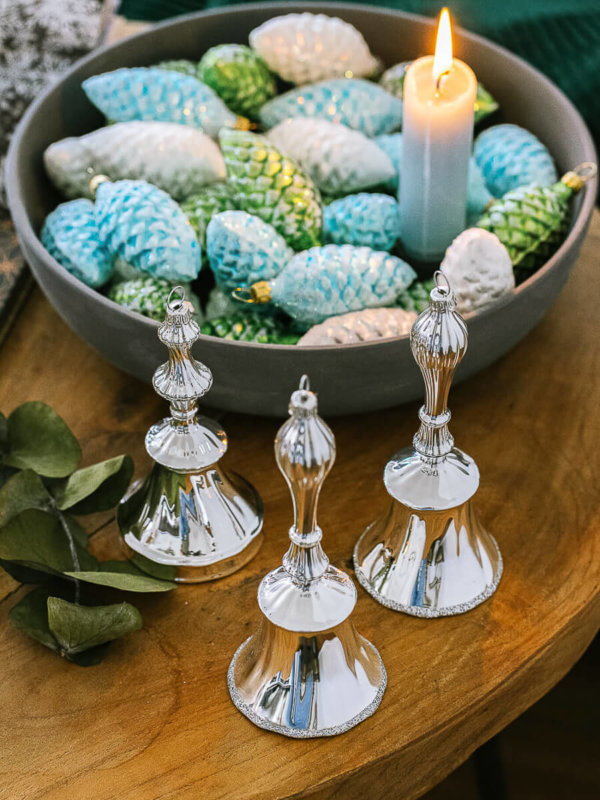 Tischglocken in Silber vor einer Schale mit Glas Tannenzapfen